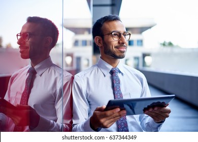 Millenial businessman leaning confidently on a dark glass wall with cityscape background