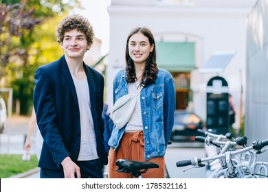 Millenial Couple Stands With Bicycle In Bike Parking. Man And Woman Take City Bicycle Vacation At Parking. Public Bikes For Rent Parked In Street. Save  Green Energy. Youth People And Cycle In Europe.