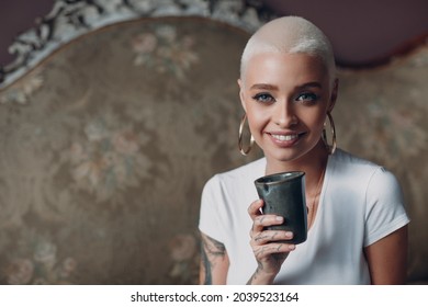 Millenial Young European English Woman With Short Blonde Hair Portrait Sitting With Cup Of Tea Or Coffee Drink On Vintage Sofa