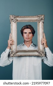 Millenial Young Man Artist With Blonde Hair On Gilded Picture Frame Portrait. Isolated On Blue Background In Studio.