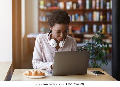 Millennial African American Girl With Headset Working On Laptop In Coffee Shop