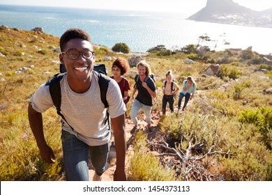 Millennial African American man leading friends hiking single file uphill on a path by the coast - Powered by Shutterstock