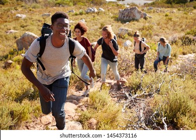 Millennial African American Man Leading Friends Hiking Single File Uphill On A Path In Countryside