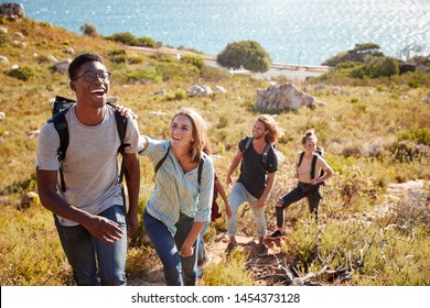 Millennial African American Man Leading Friends Hiking Single File Uphill On A Path By The Coast