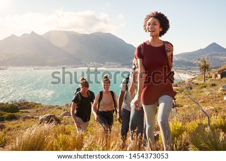 Millennial African American woman leading friends on an uphill hike by the coast, close up