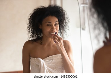 Millennial african American woman in shower towel look in mirror clean brush tooth in bathroom, young biracial female perform morning face care routine, do cleanup oral hygiene, use toothbrush - Powered by Shutterstock