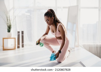 Millennial African American Woman In Sportswear Wiping Yoga Mat After Training At Home Gym, Empty Space. Fit Young Black Female Using Detergent Spray, Cleaning Equipment After Fitness Class