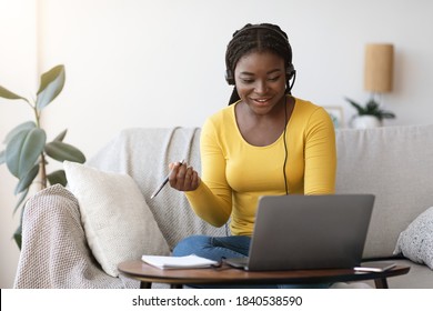 Millennial African Lady In Headset Watching Webinar On Laptop At Home, Having Online Training, Studying With Computer And Taking Notes To Notepad, Enjoying Distance Learning, Copy Space