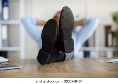 Millennial Arab office employee relaxing after work, putting legs on table at workplace, focus on feet. Young entrepreneur resting with hands behind his head, taking break from job