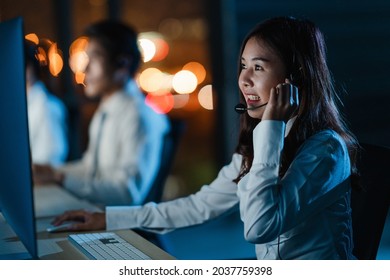 Millennial Asia young call center team or customer support service executive using computer and microphone headset working technical support in late night office. Telemarketing or sales job concept.