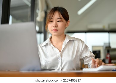 Millennial Asian businesswoman focusing on her project assignment, using laptop computer, working in her office room. - Powered by Shutterstock