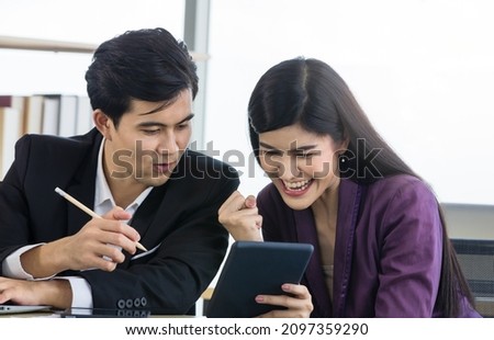 Millennial Asian happy professional successful male businessman and female businesswoman colleague in formal outfit sitting at working desk take break holding tablet have fun conversation together.