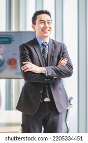 Millennial Asian Happy Successful Professional Male Businessman Entrepreneur In Formal Suit Standing Smiling In Company Office Meeting Room With Big Screen Monitor