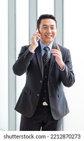 Millennial Asian Happy Successful Professional Male Businessman Entrepreneur In Formal Suit Standing Smiling In Company Office Meeting Room With Big Screen Monitor