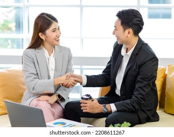 Millennial Asian professional successful businessman in formal suit sitting on sofa smiling holding disposable hot coffee cup shaking hands greeting with businesswoman customer in office meeting room. - Shutterstock ID 2208611267