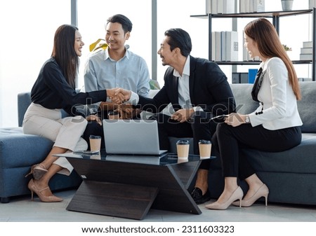 Millennial Asian professional successful businessman in formal suit sitting with female secretary shaking hands with clients after job negotitation acheivement agreement in company office living room.