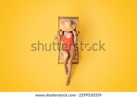 Millennial asian woman in swimsuit and hat sleep on deck chair, enjoy free time, isolated on orange studio background, top view, unrecognizable. Ad and offer at summer, rest and relax