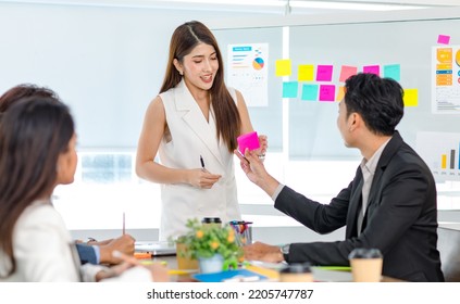 Millennial Asian young professional businesswoman presenter standing talking presenting company business model data report on glass board to male and female employee colleagues in office meeting room. - Shutterstock ID 2205747787
