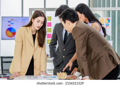 Millennial Asian young professional successful male and female businessman businesswoman worker employee in formal suit standing discussing brainstorming together at working desk in company office. - Shutterstock ID 2156311529