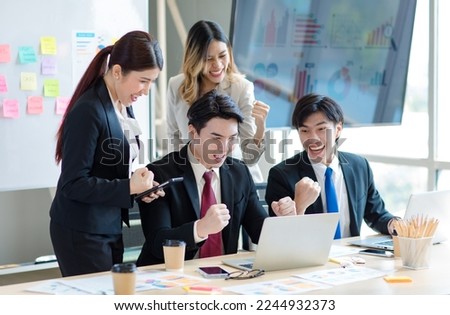 Millennial Asian young professional successful  businessman in formal suit laughing holding fists up celebrating with female and male businessman colleagues after winning job acheivement deal done
