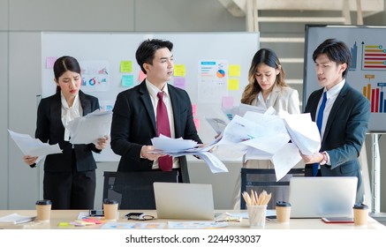 Millennial Asian young upset stressed male female businessmen businesswomen employee in formal suit working overload overtime with strategy paperwork documents together in company office meeting room. - Powered by Shutterstock