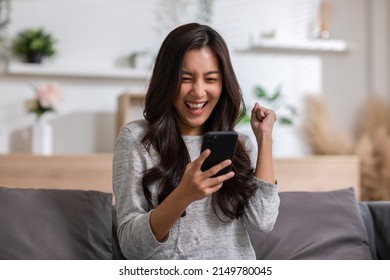 Millennial Asian Young Woman Looking Mobile Phone Laughing With Good News Or Discount Voucher For Shopping Online At Home.Happy And Cheerful Woman Looking On Cellphone App Read Message Feel Excited