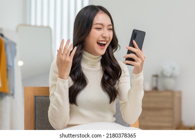 Millennial Asian Young Woman Looking Mobile Phone Laughing With Good News Or Discount Voucher For Shopping Online At Home.Happy And Cheerful Woman Looking On Cellphone App Read Message Feel Excited