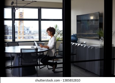 Millennial black businesswoman working alone in an office meeting room, seen through glass wall