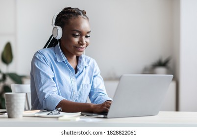 Millennial Black Female Employee Working With Laptop And Listening Music In Office, Wearing Headphones, African Woman Sitting At Desk Typing On Computer Keyboard, Answering Emails, Copy Space