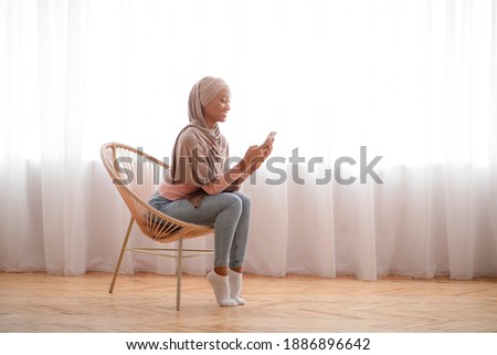 Millennial black lady in hijab using cellphone at home, working or studying remotely, free space. African American woman in Muslim headscarf checking email, sending message, having online video call