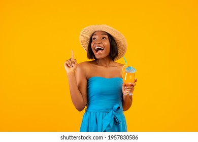 Millennial black lady with yummy tropical cocktail screaming WOW and pointing upwards on orange studio background. Excited African American woman advertising summer sale or promo