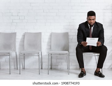 Millennial black man reading his resume while waiting for job interview at office hall, empty space. African American work candidate with CV applying for position in big company
