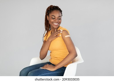 Millennial Black Woman Getting Vaccinated Against Covid, Showing Arm With Bandage On Grey Studio Background. African American Female Smiling After Receiving Coronavirus Vaccine Shot