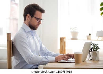 Millennial businessman with eyeglasses using computer sitting at the desk in office room or home feels confident typing writing a business letter, responding to an email, fruitful working day concept - Shutterstock ID 1189954918