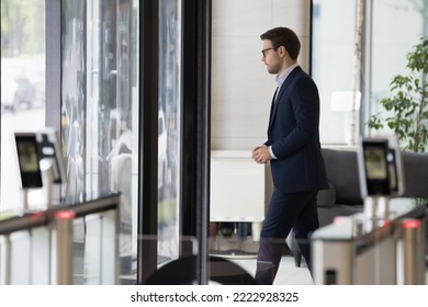 Millennial businessman in formal suit leaving office building area, passes through doorway, security gateway and electronic card reader, working day ended, going at lunch break in modern workplace - Shutterstock ID 2222928325