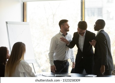 Millennial businessman setting apart two aggressive multiracial coworkers, starting fighting at office. Mixed race young colleagues quarreling shouting at each other, misbehaving during meeting. - Shutterstock ID 1523258309
