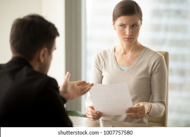 Millennial businesswoman with skeptical facial expression holding contract document and listening unconvincing offer of business partner. Suspicious terms of agreement, doubtful investor, fraud, scam