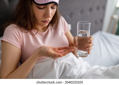 Millennial Cauasian Woman With Water Taking Pills, Feeling Sick, Using Meds At Home. Young Lady In Sleep Mask Treating Her Illness, Drinking Tablets, Vitamins Or Supplements