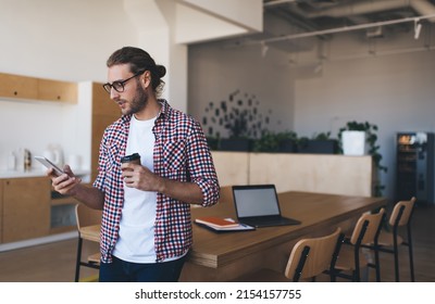 Millennial caucasian businessman using and watching on smartphone. Concept of modern successful man. Young focused male entrepreneur in glasses standing and working at table in open space office - Powered by Shutterstock