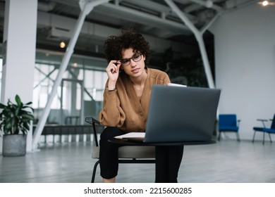 Millennial Caucasian Businesswoman Watching Something On Laptop During Work. Concept Of Modern Successful Woman. Young Focused Girl In Glasses Sitting In Armchair At Table In Open Space Office