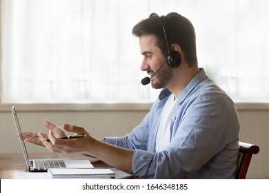 Millennial Caucasian male worker in headset talk consult client online using wireless internet on laptop, man call center agent or telemarketer in earphones speak with customer working on computer - Shutterstock ID 1646348185