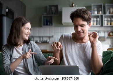Millennial couple having fun listening to music online on computer application, smiling teenagers relaxing enjoying favorite songs dancing to new audio tracks sitting on couch at home with laptop