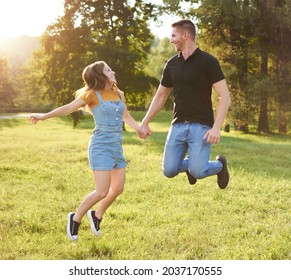 Millennial couple holding each other's hand and jumping together outdoors in a park - Happy people lifestyle concept
