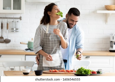 Millennial couple preparing healthy vegetarian salad laughing enjoying process and time with better half on modern cozy kitchen, cooking together during first dating, relish activity at home concept
