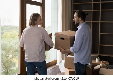 Millennial Couple Talking While Carrying Boxes With Belongings Into Living Room On Move-in Day, Start Living Together In Rented Or Bought New First Property. Bank Loan, Tenancy, Cohabitation Concept