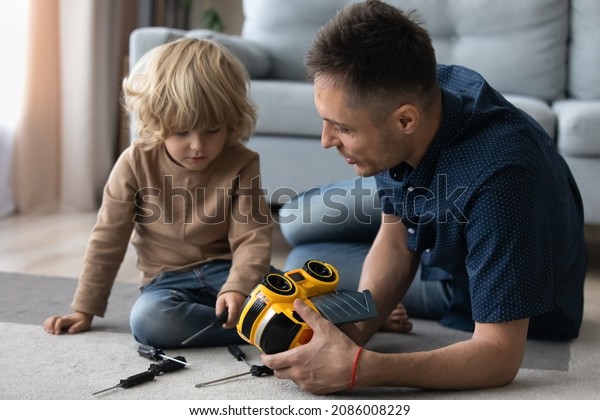 Millennial dad and cute preschooler son engaged in\
motor mechanic games on heating floor, repairing toy plastic car\
with screwdrivers. Father and kid playing together, enjoying\
activities at home