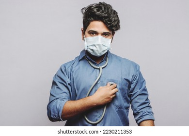 A millennial doctor uses a stethoscope to listen to the beating of his own heart. A doctor examining his own heartbeat and looking at the camera in grey background. - Shutterstock ID 2230211353