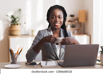 Millennial employee. Smiling black secretary drinking coffee at workplace in modern office and looking at camera, copy space - Shutterstock ID 1584668518