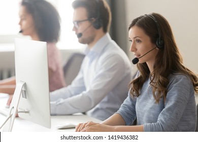 Millennial Female Call Center Agent Wear Headset With Microphone Consult Customer Online On Pc In Coworking Space, Focused Woman Employee In Earphones Busy Working On Computer In Shared Office