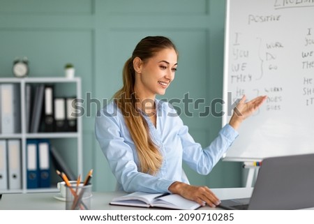 Millennial female English teacher having video conference chat with students, talking to laptop webcamera, explaining grammar rules and smiling